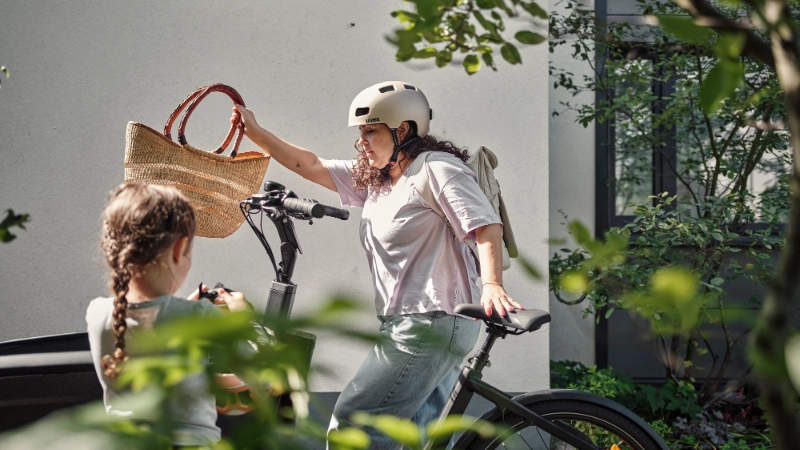Eine Frau holt einen Korb aus dem Lastenrad, im Vordergrund schaut ein Kind zu