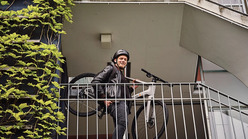 JobRadler trägt Fahrrad die Treppe herunter und lacht in Kamera