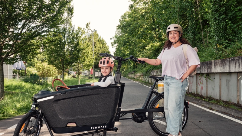 JobRadlerin posiert stolz neben ihrem Lastenrad mit Kind auf der Fahrradstraße