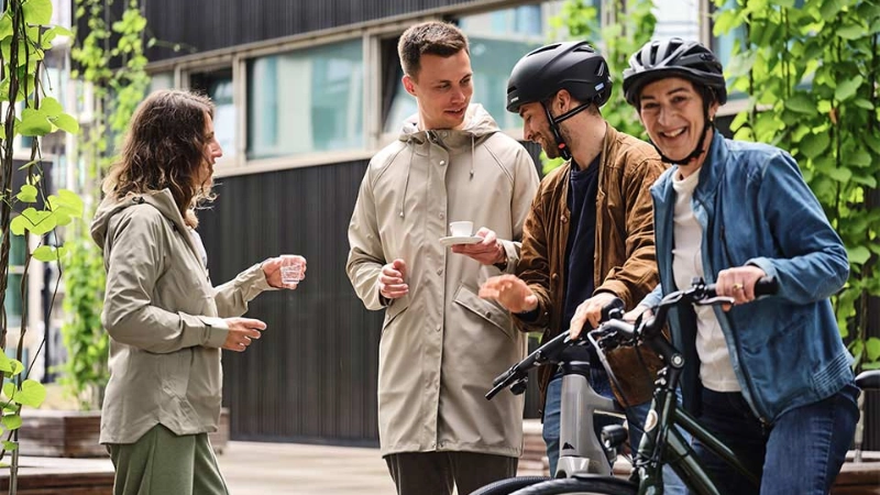 Ein JobRad Team aus vier Personen trinkt Kaffee auf dem JobRad-Campus, eine Frau aus dem Team sitzt auf dem Fahrrad