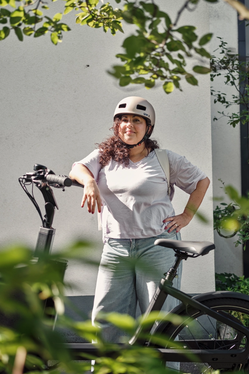 Frau mit Locken lehnt am JobRad, im Vordergrund Pflanzen