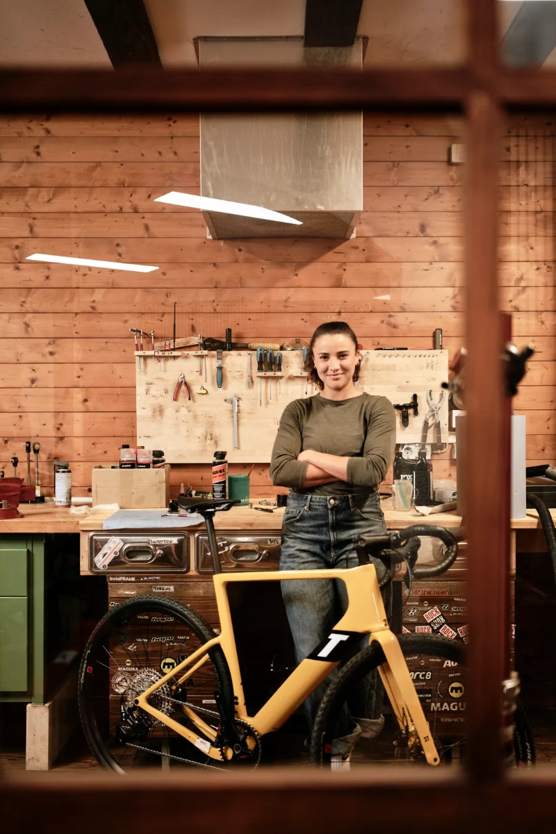 Mechanikerin steht mit Bike in der Werkstatt und schaut selbstbewusst in die Kamera