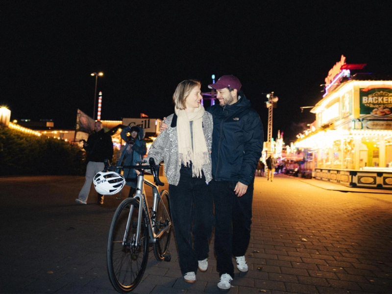 Paar geht nach Hause, im Hintergrund Lichter eines Jahrmarkts
