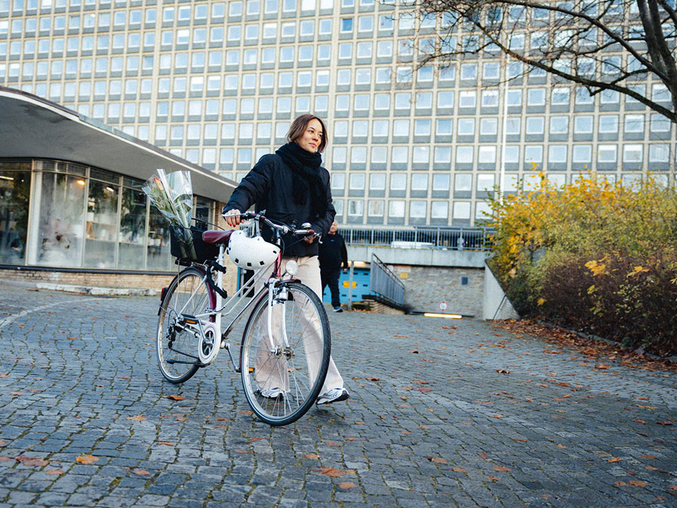 Junge Frau schiebt zufrieden ihr Fahrrad vor einem Bürogebäude