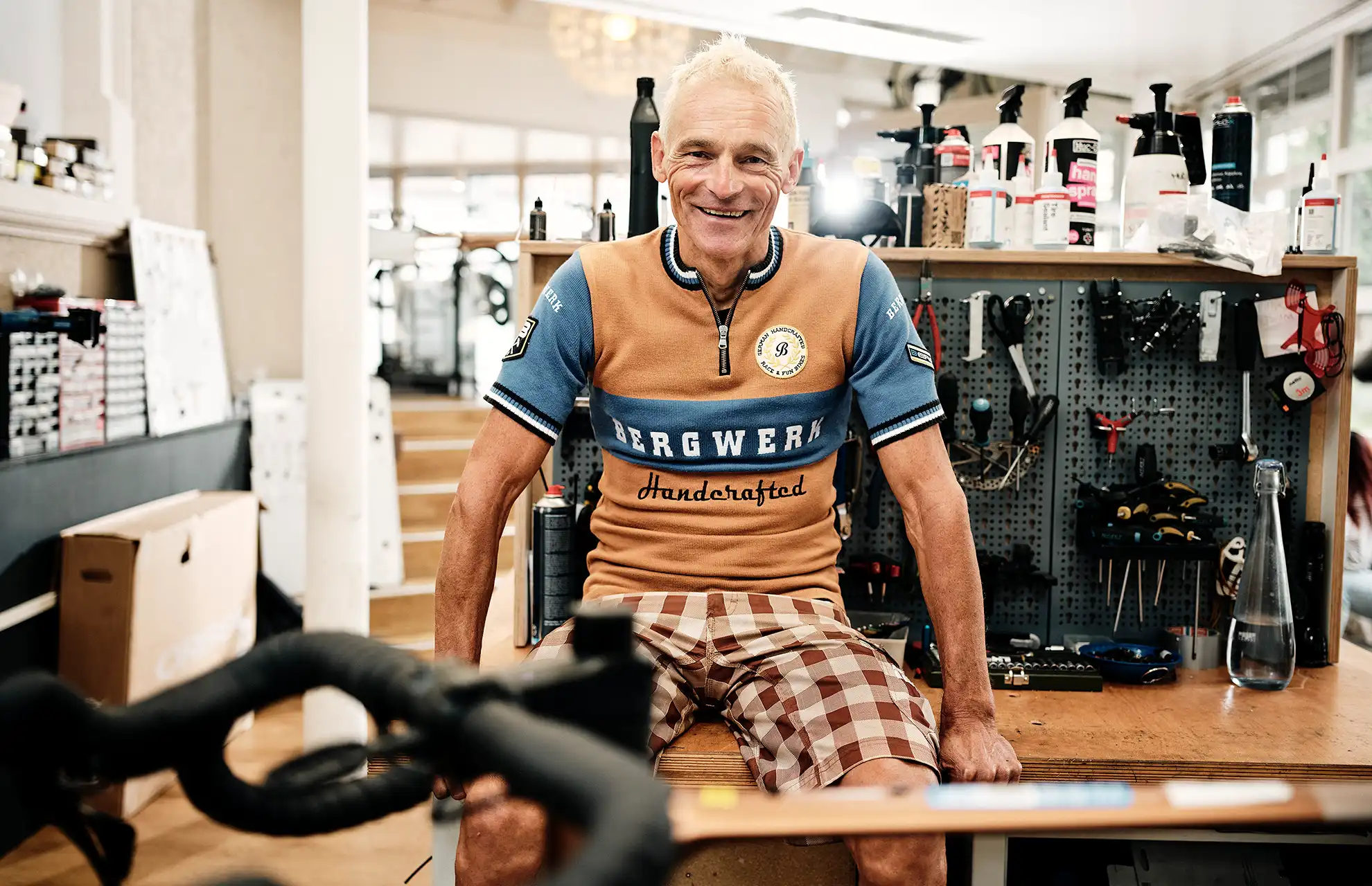 Mann sitzt auf Werkbank im Fahrrad Fachhandel und lächelt in die Kamera